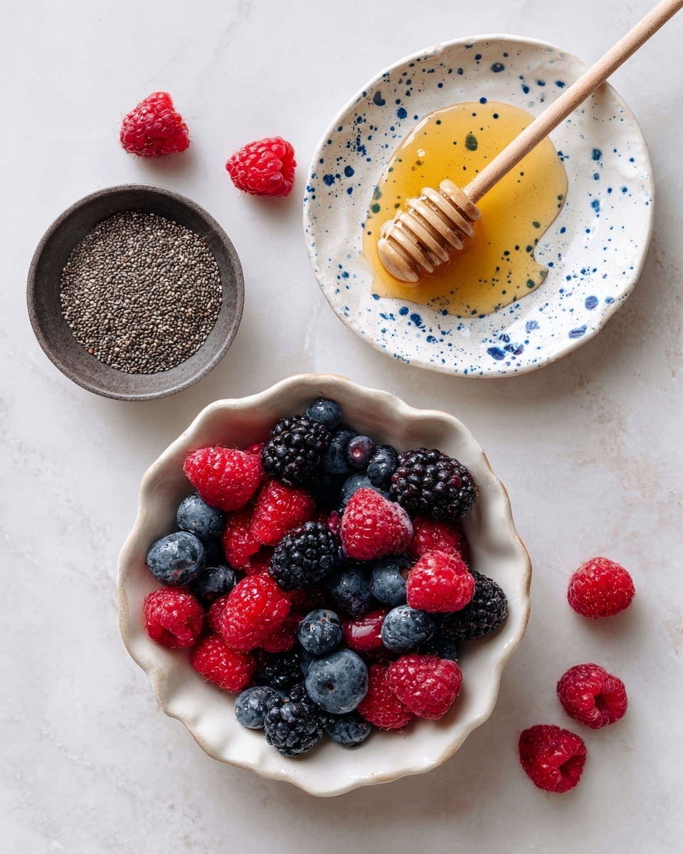 The image shows three main items arranged on a white marbled surface. In the center bottom, there is a white, scalloped bowl filled with a mix of frozen berries including red raspberries, black blackberries, and dark blue blueberries, creating a colorful mix of red, black, and blue. To the top right of the bowl, a white plate with blue speckles holds golden honey with a wooden honey dipper resting diagonally in it. To the left of the honey, a small dark bowl is filled with tiny, round, black chia seeds. Around the bowls and plate, scattered fresh raspberries and blueberries add bright red and deep blue colors, enhancing the natural and fresh feel of the scene. Photo taken with an iphone --ar 4:5 --v 7