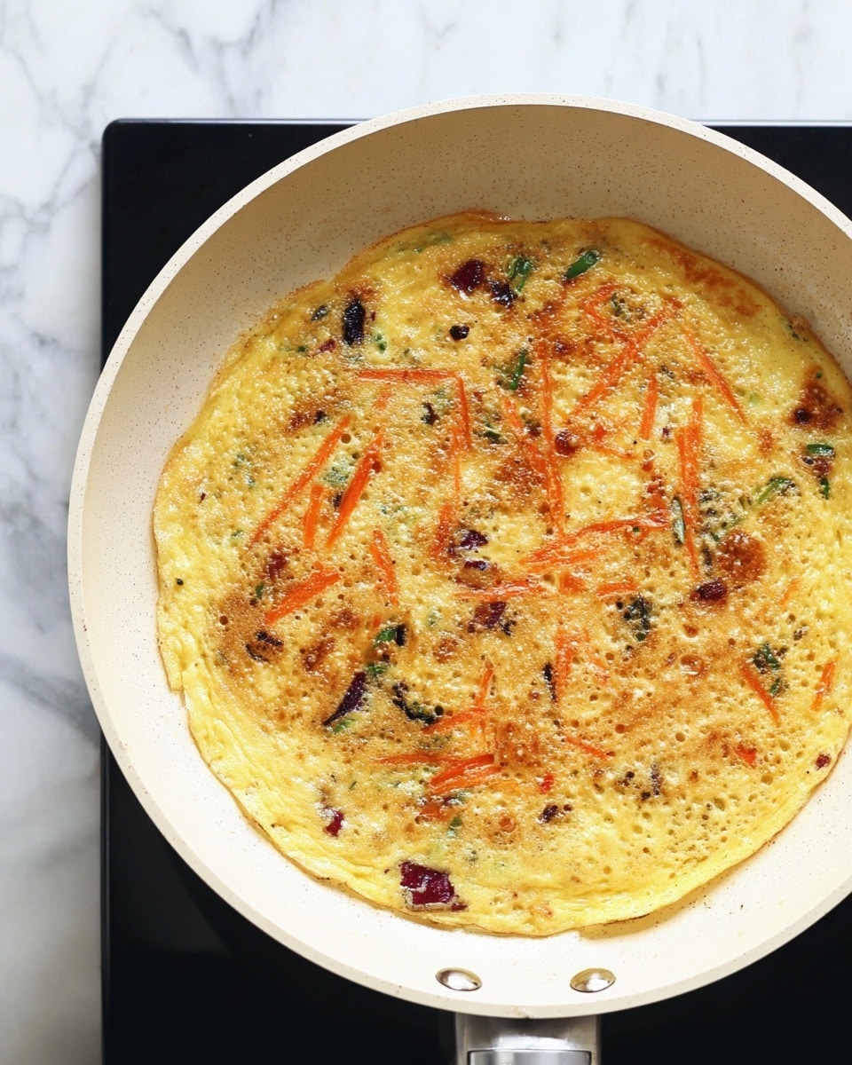 A light yellow omelette is cooking in a white nonstick pan, spread out evenly in one flat layer with small bubbles forming on its surface. Mixed inside the omelette are pieces of dark purple-red vegetables and thin strips of bright orange carrots scattered evenly throughout. The texture shows slight browning with a few golden brown spots, especially near the center, giving it a slightly crisp look. The pan rests on a black stovetop with a white marbled surface around it photo taken with an iphone --ar 4:5 --v 7