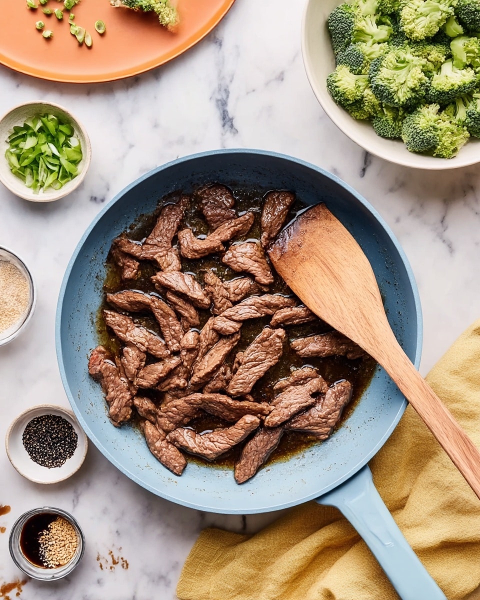 The image shows a light blue frying pan filled with many pieces of cooked brown meat strips in oil, sitting on a white marbled surface. A wooden spatula rests inside the pan on the right side, lying over the meat. Around the pan, there is a white bowl on the top right filled with green broccoli florets, an orange plate on the top left holding chopped green onions, and small bowls containing black pepper, sesame seeds, and a dark sauce spread out on the marbled surface. A yellow cloth napkin is partially visible under the pan on the right side. Photo taken with an iphone --ar 4:5 --v 7