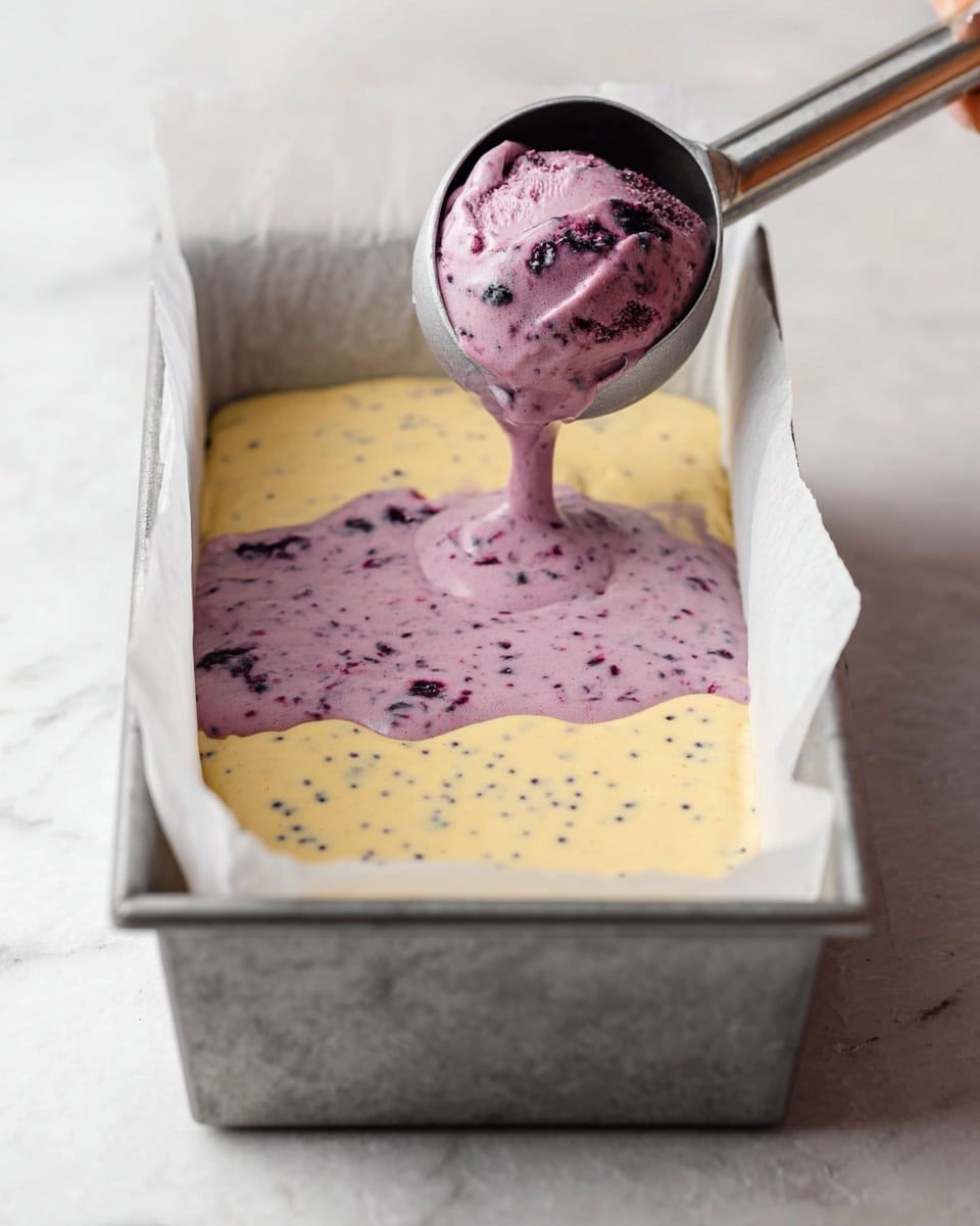 A metal loaf pan lined with white parchment paper sits on a white marbled surface. Inside the pan, there is a first layer of pale yellow batter speckled with small dark dots. Above this layer, a woman's hand is using a metal ice cream scoop to pour a thick, creamy purple batter with visible small dark berries over the yellow batter, creating a second layer with uneven edges. The photo appears soft and natural, focusing closely on the layered batters in the pan. photo taken with an iphone --ar 4:5 --v 7